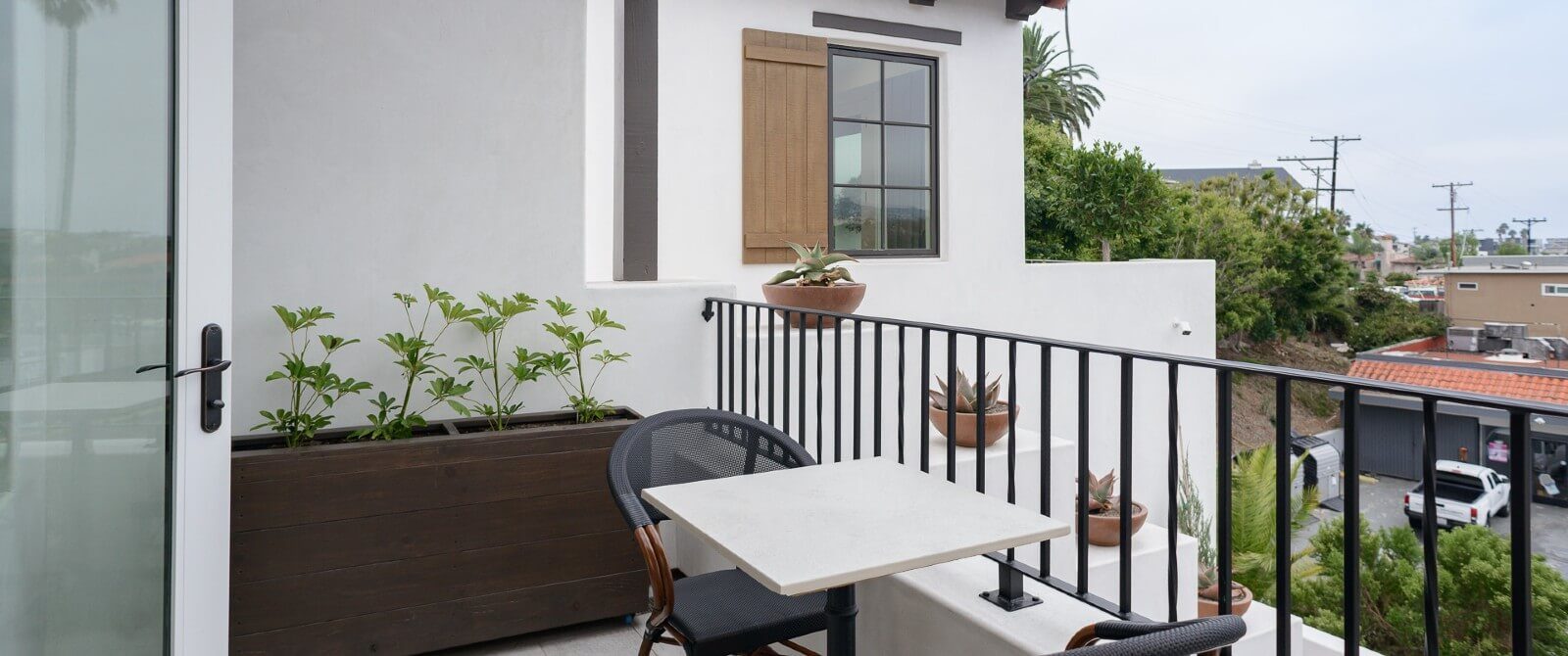 Spacious outdoor patio with table, two chairs, wrought iron railing and green plants