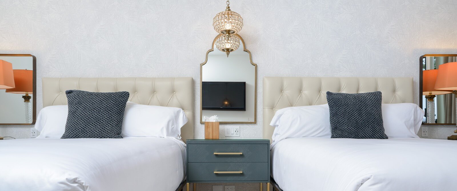 Two queens in white linens with leather tufted headboards with side table and decorative mirror