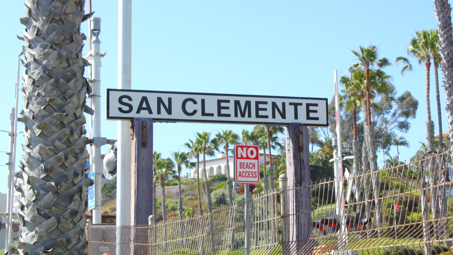 Street sign for San Clemente near a fence and palm trees