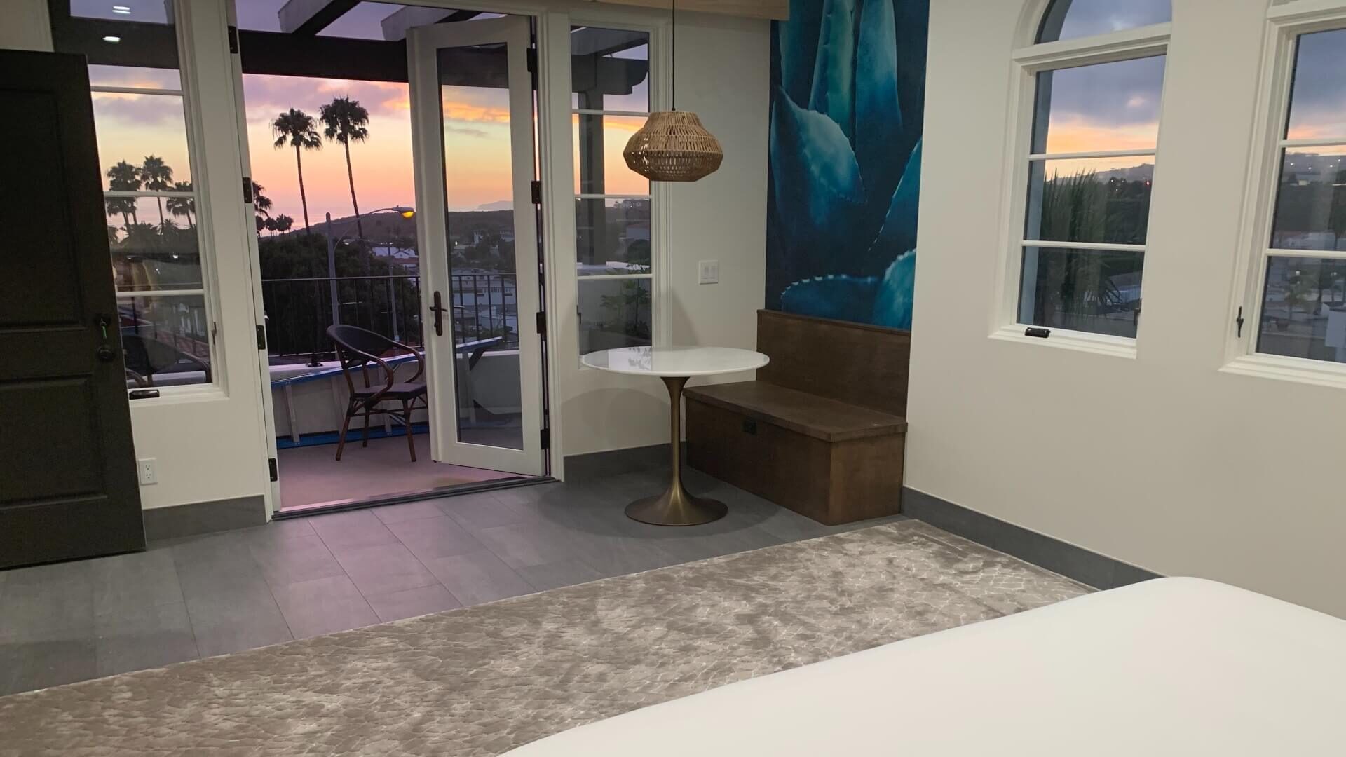 Large bedroom with French doors leading to outdoor patio with views of palm trees and a sunset sky
