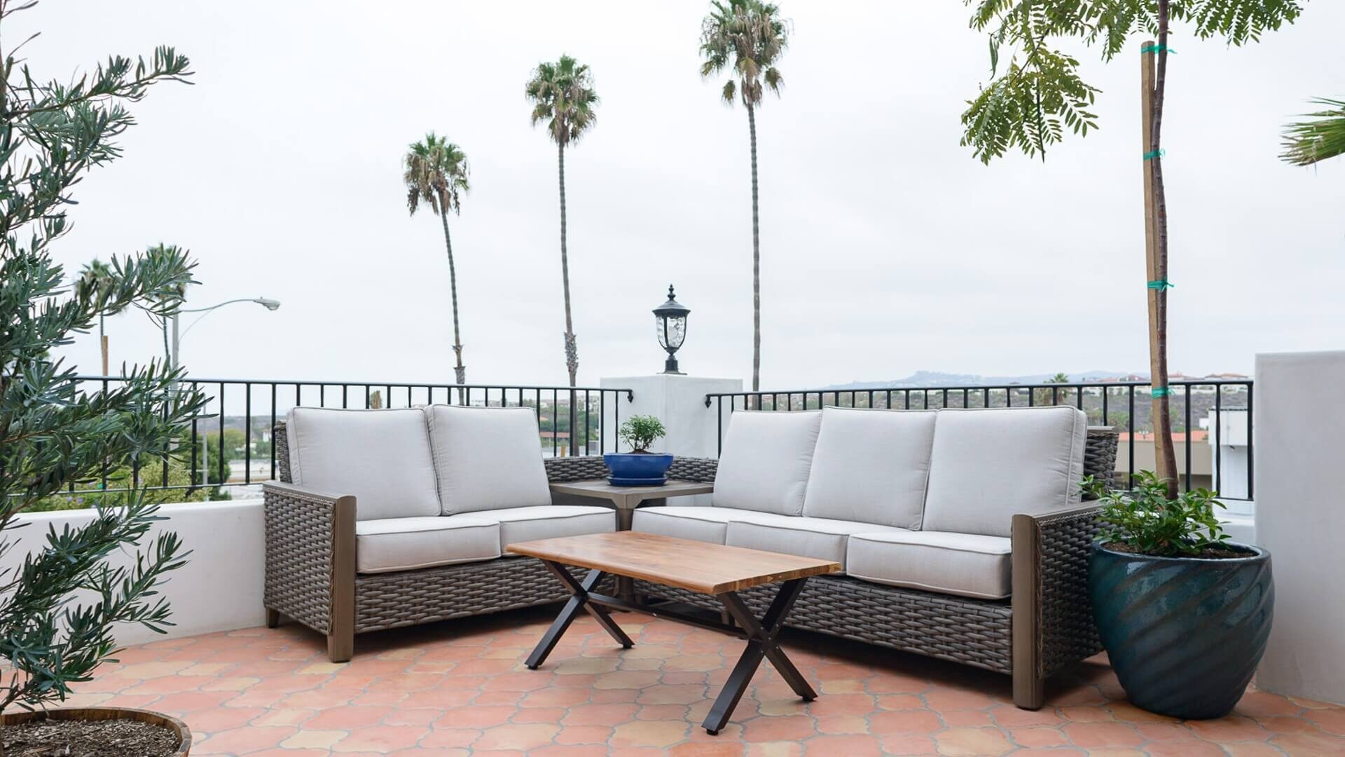 Beautiful outdoor patio with wicker seating, table, black railing and palm trees in the background