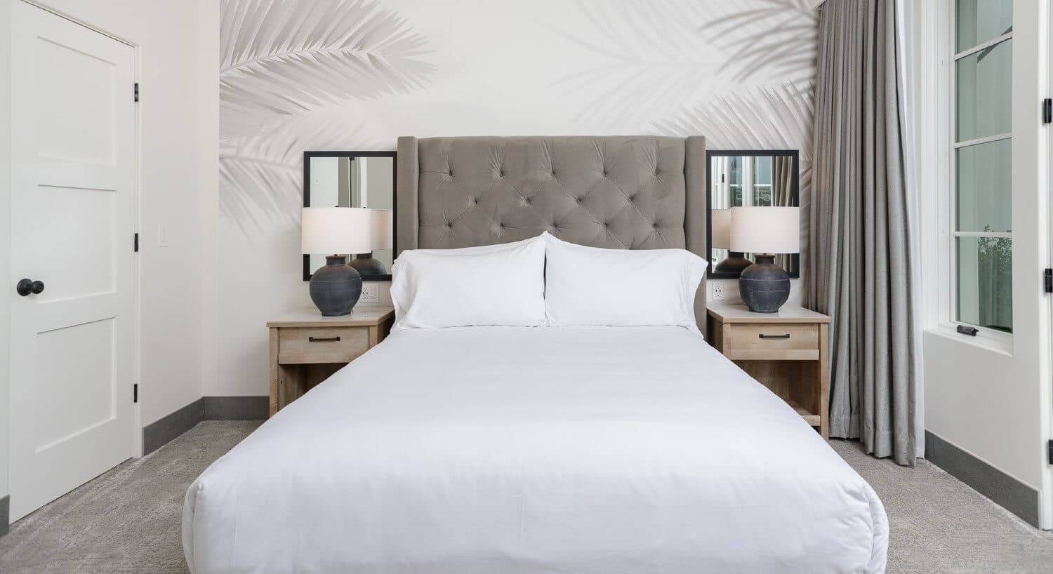 King bed with large tufted headboard, side tables with lamps and mirrors and decorative wallpaper