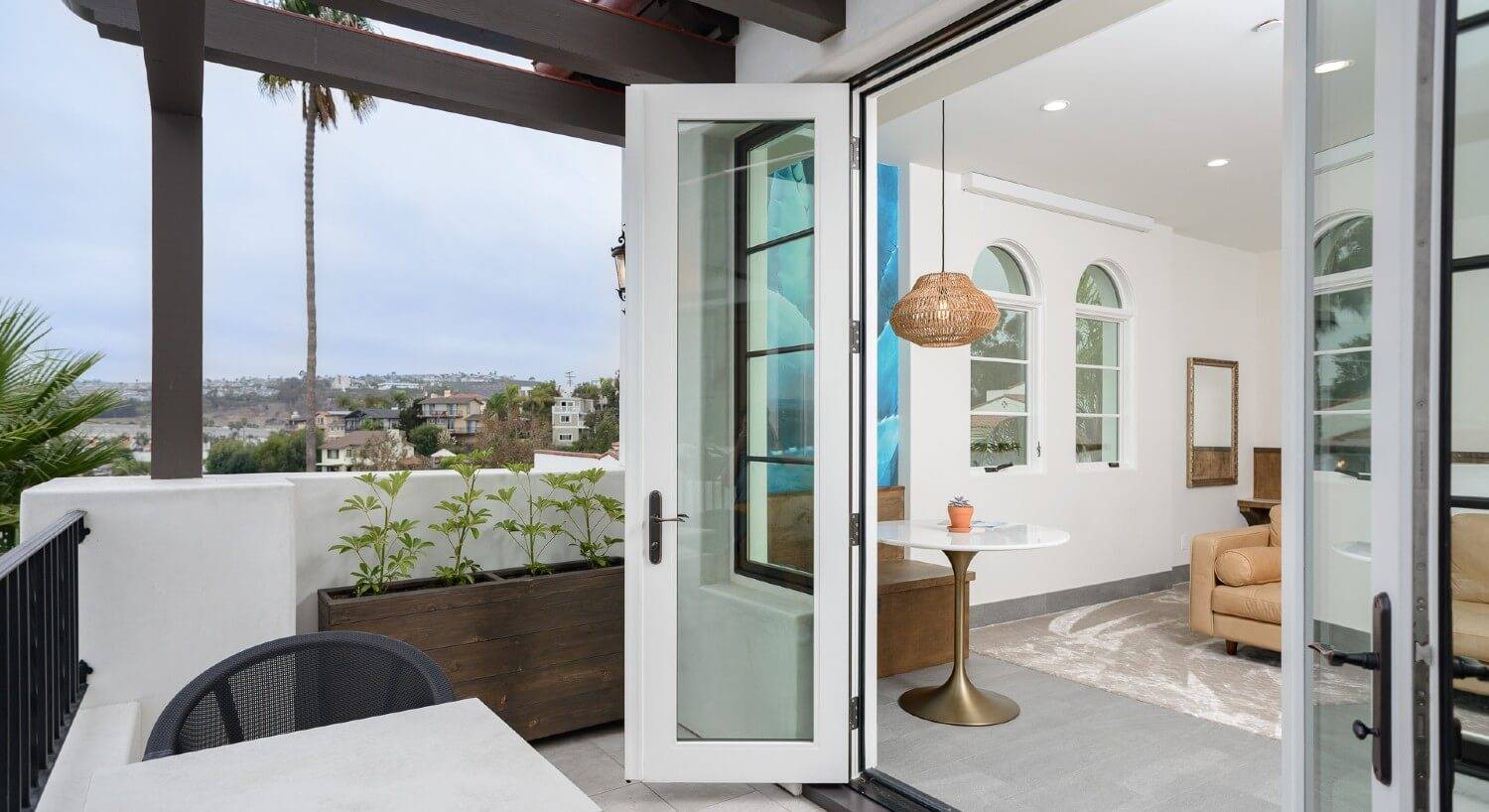 Large French doors open to an outdoor patio overlooking a city and inside of a spacious bedroom