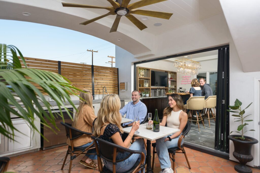 Four people gathered at a table having fun and drinking champagne with two people in the background sitting at the bar talking